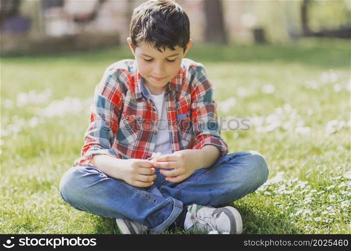 Cheerful boy portrait sitting on city park grass while looking at camera