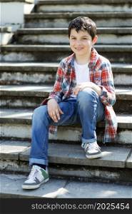 Cheerful boy sitting on bleachers at city park while looking at camera