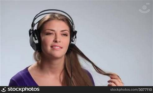 Cheerful brunette girl relaxing listening music with her headset on white. Young stunning woman enjoying music, twisting her amazing long hair around finger and gently touching her neck while listening to the music in headphones.