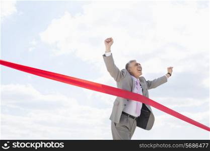 Cheerful businessman crossing finish line against sky