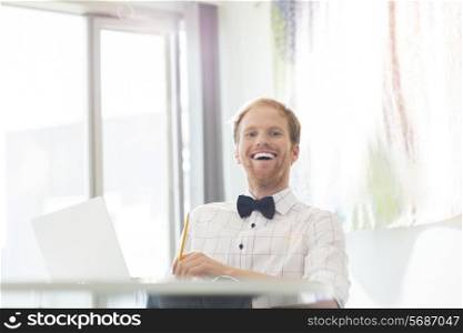 Cheerful businessman sitting at desk in creative office
