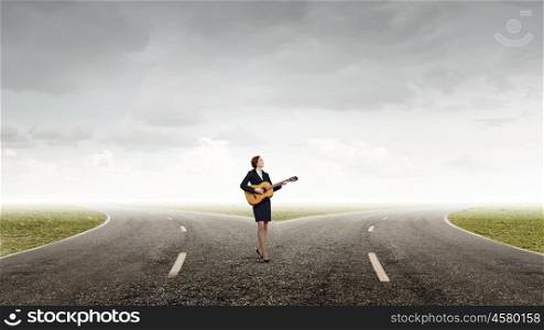 Cheerful businesswoman standing on road and playing guitar. Playing melody of success