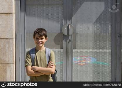 Cheerful child carrying his backpack standing in front of the school.