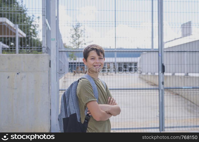 Cheerful child carrying his backpack standing in front of the school.