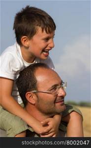 Cheerful child plays in the countryside on father?s shoulders