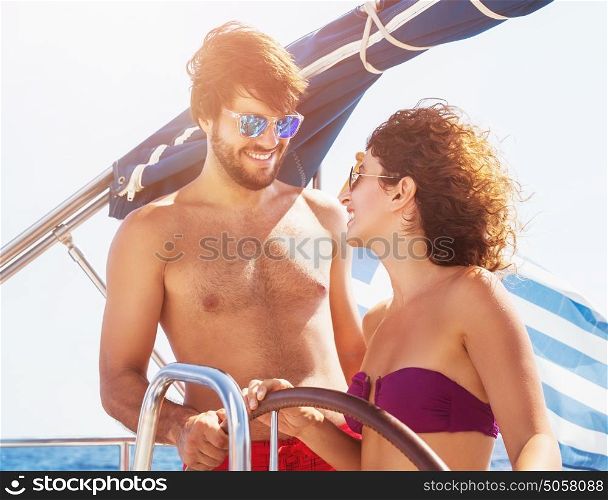 Cheerful couple driving sailboat, handsome guy and cute girl laughing and looking with love on each other, enjoying active summer vacation