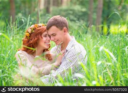 Cheerful couple having fun outdoors, beautiful young family sitting on green grass in the park and laughing, enjoying time spending together