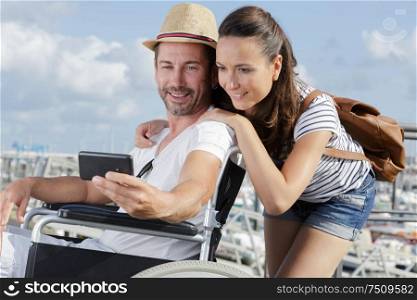 cheerful couple in wheelchair doing a selfie outdoors