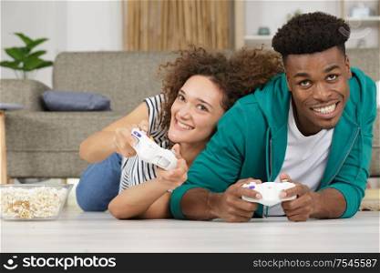 cheerful couple playing video games while lying on a carpet