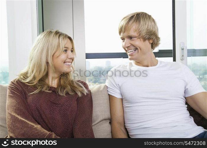 Cheerful couple sitting on sofa and looking at each other at home