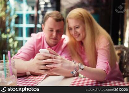 Cheerful couple surfing the web, looking a photo on smartphone, summer outdoor cafe