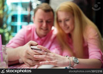 Cheerful couple surfing the web, looking a photo on smartphone, summer outdoor cafe