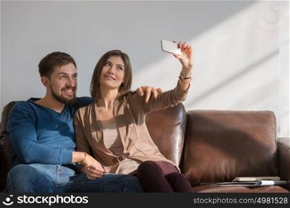 Cheerful couple taking a selfie with a smartphone at home sitting on couch