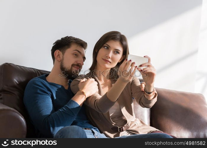 Cheerful couple taking a selfie with a smartphone at home sitting on couch