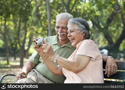 Cheerful couple using digital camera at park