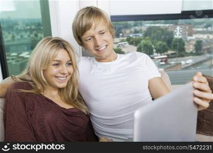 Cheerful couple using laptop in living room at home