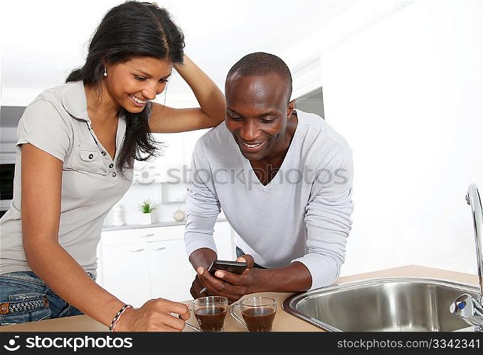 Cheerful couple using smartphone while taking coffee