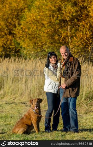 Cheerful couple with dog in park autumn sunset