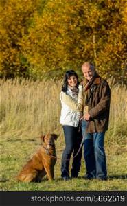Cheerful couple with dog in park autumn sunset