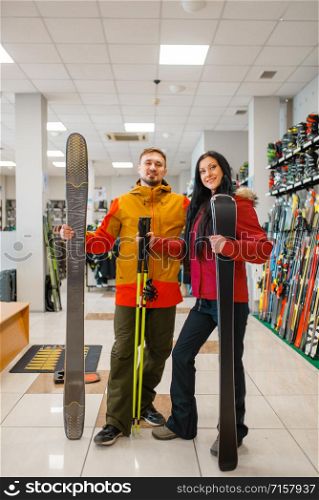 Cheerful couple with skis in hands, shopping in sports shop. Winter season extreme lifestyle, active leisure store, customers buying skiing equipment