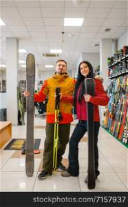Cheerful couple with skis in hands, shopping in sports shop. Winter season extreme lifestyle, active leisure store, customers buying skiing equipment