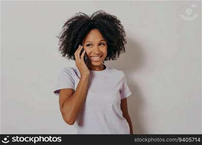 Cheerful dark-skinned woman enjoys phone conversation, smiles, hears good news. Studio portrait. Isolated on white background