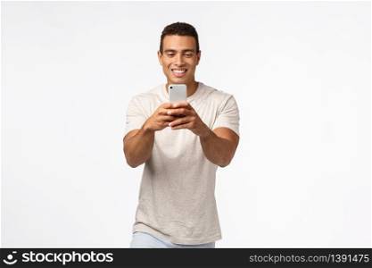 Cheerful, excited good-looking brazilian man with strong muscles, holding smartphone, looking enthusiastic gadget screen, record video, attend amusing event, taking photos on telephone camera.. Cheerful, excited good-looking brazilian man with strong muscles, holding smartphone, looking enthusiastic gadget screen, record video, attend amusing event, taking photos on telephone camera