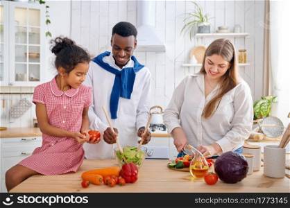 Cheerful family cooking vegetable salad on breakfast. Mother, father and their daughter on the kitchen in the morning, good relationship. Cheerful family cooking salad on breakfast