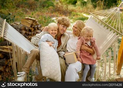 Cheerful family having fun on hammock, summer camping. Couple with children travel in camp car, nature and forest on background. Campsite adventure, travelling lifestyle, vacation on motorhome. Cheerful family having fun on hammock, camping