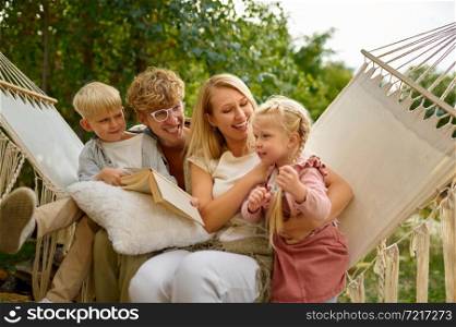 Cheerful family having fun on hammock, summer camping. Couple with children travel in camp car, nature and forest on background. Campsite adventure, travelling lifestyle, motorhome vacation. Cheerful family having fun on hammock, camping