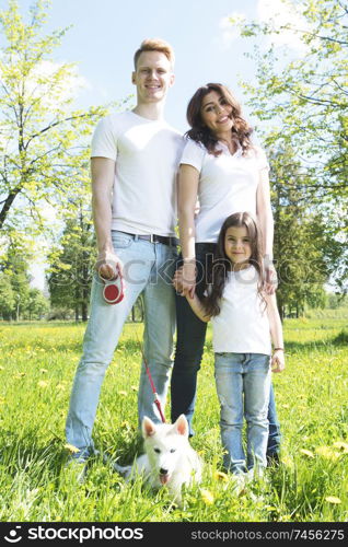 Cheerful family in summer sunny park walking on grass with dog. Cheerful family in park
