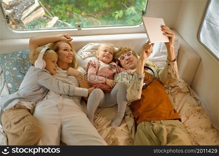 Cheerful family lying in bed in motorhome, summer camping. Couple with children travel in camp car, trailer interior on background. Campsite adventure, travelling lifestyle, vacation on rv car. Cheerful family lying in bed in motorhome, camping
