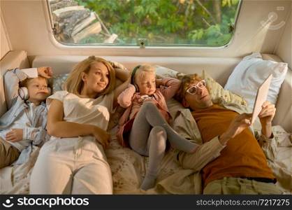 Cheerful family lying in bed in motorhome, summer camping. Couple with children travel in camp car, trailer interior on background. Campsite adventure, travelling lifestyle, vacation on rv car. Cheerful family lying in bed in motorhome, camping