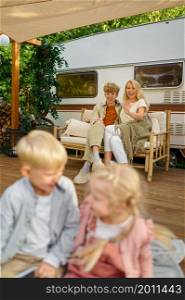 Cheerful family relaxing at the motorhome, summer camping. Parents with children travel in camp car, nature and forest on background. Campsite adventure, travelling lifestyle, campers. Cheerful family relaxing at the motorhome, campers