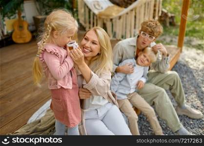 Cheerful family resting at the motorhome, summer camping. Parents with children travel in camp car, nature and forest on background. Campsite adventure, travelling lifestyle. Cheerful family resting at the motorhome, camping