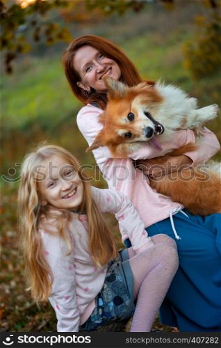cheerful family - smiling mom and daughter and corgi fluffy in the autumn park.