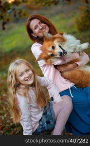 cheerful family - smiling mom and daughter and corgi fluffy in the autumn park.