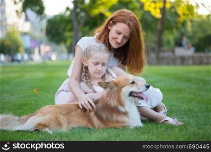 cheerful family - smiling mom and daughter and corgi fluffy sit on the lawn