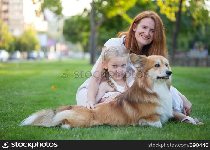 cheerful family - smiling mom and daughter and corgi fluffy sit on the lawn