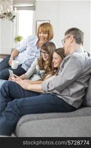 Cheerful family using tablet PC on sofa at home
