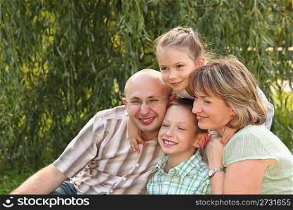 cheerful family with two children in early fall park. father, mother, little boy and girl is sitting near osier