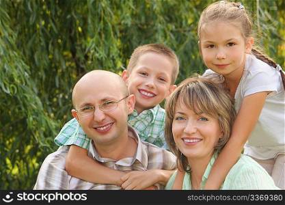 cheerful family with two children in early fall park. son is embracing father and daughter is embracing mother