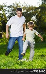Cheerful father and son catch up with a football in park