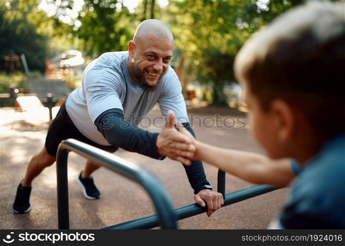 Cheerful father and son, sport training on playground outdoors. The family leads a healthy lifestyle, fitness workout in summer park. Cheerful father and son, sport training outdoors