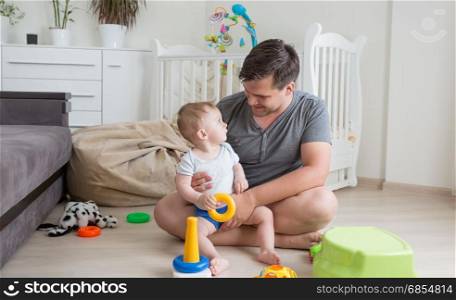 Cheerful father playing with his baby boy on floor at living room