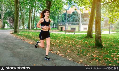 Cheerful female athlete running through a park. Female athlete running through a park