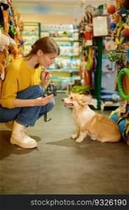 Cheerful female customer buying dog harness in pet store. Young woman showing new leash for her corgi puppy. Cheerful female customer buying dog harness in pet store