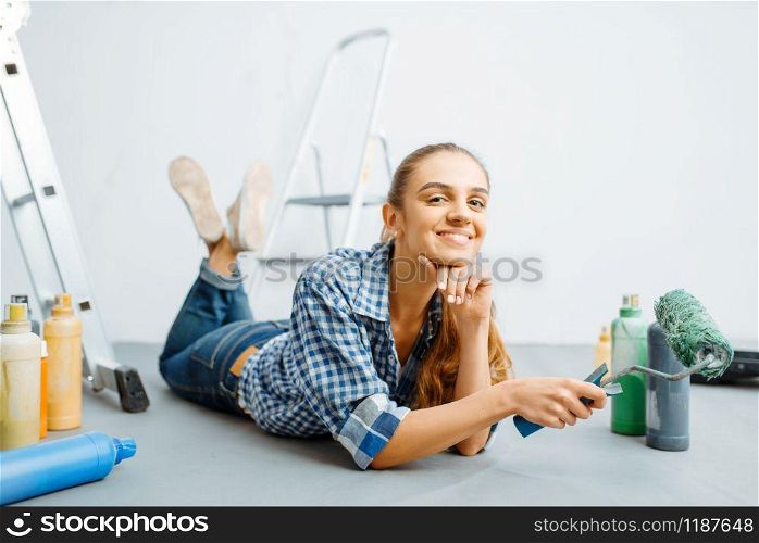 Cheerful female house painter lies on the floor. Home repair, happy woman doing appartment renovation, room decoration renovating. Cheerful female house painter lies on the floor