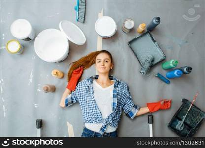 Cheerful female house painter lies on the floor, top view. Home repair, happy woman doing appartment renovation, room decoration renovating. Female house painter lies on the floor, top view