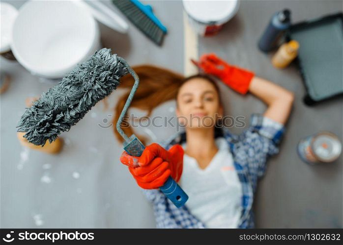 Cheerful female house painter lies on the floor, top view. Home repair, happy woman doing appartment renovation, room decoration renovating. Female house painter lies on the floor, top view